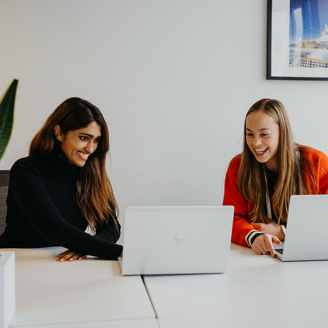 Two employees smiling and looking at a laptop