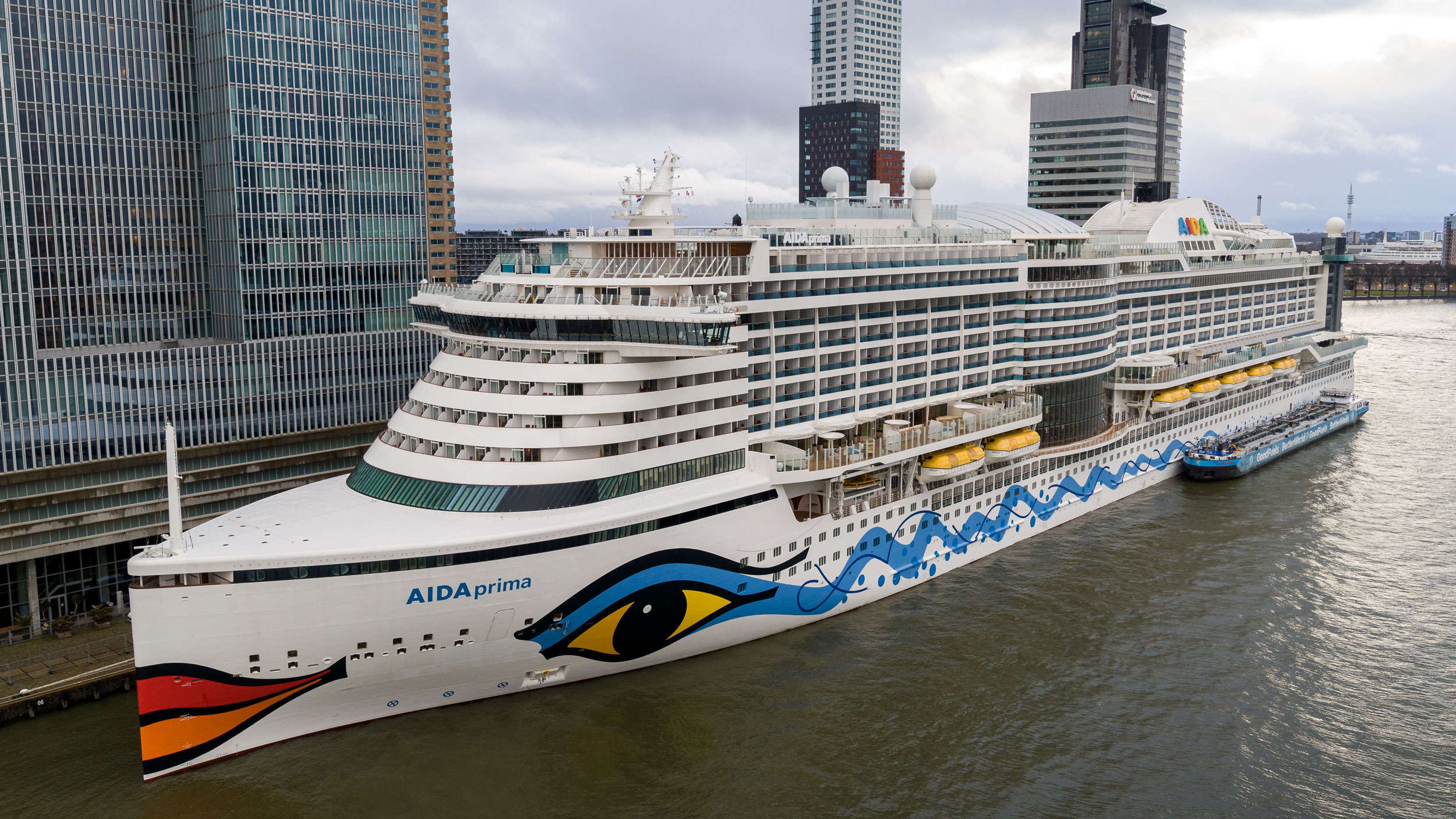 A cruise vessel moored in a port, being supplied with sustainable biofuel by a bunker barge